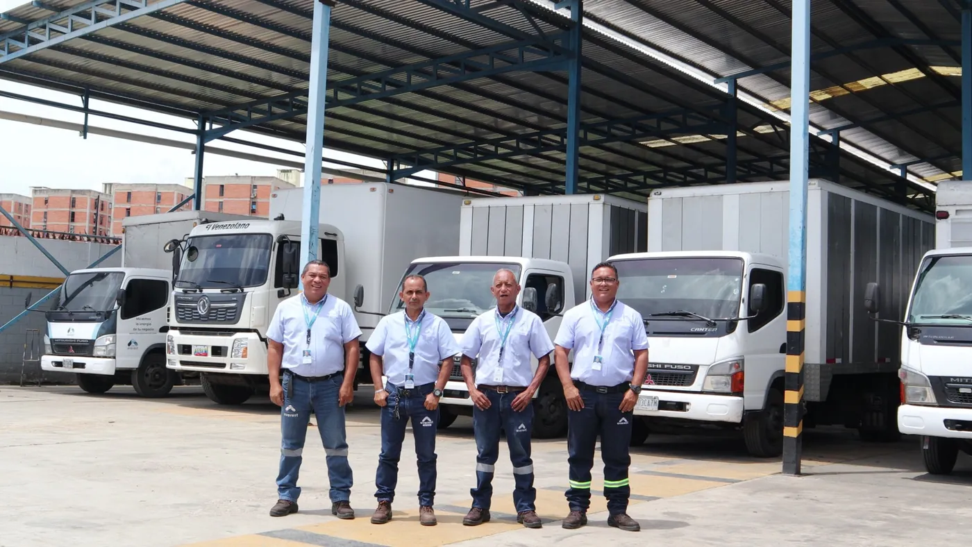 Cuatro Representantes de Everest con uniforme, de pie frente a los camiones de la flota